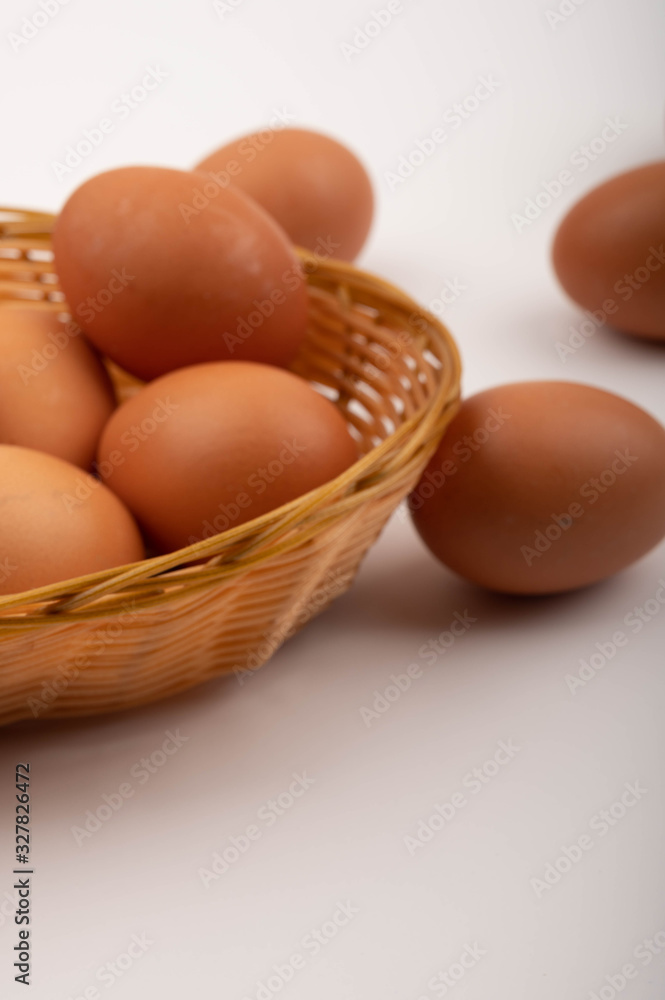 Chicken eggs in a wicker basket and scattered on a white background. Close up. Chicken eggs in a wicker basket and scattered on a white background. Close up.