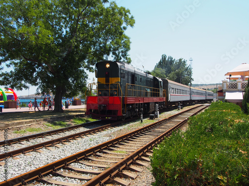 Locomotive with three cars going along the railway track laid along the waterfront of the seaside town , summer day.
