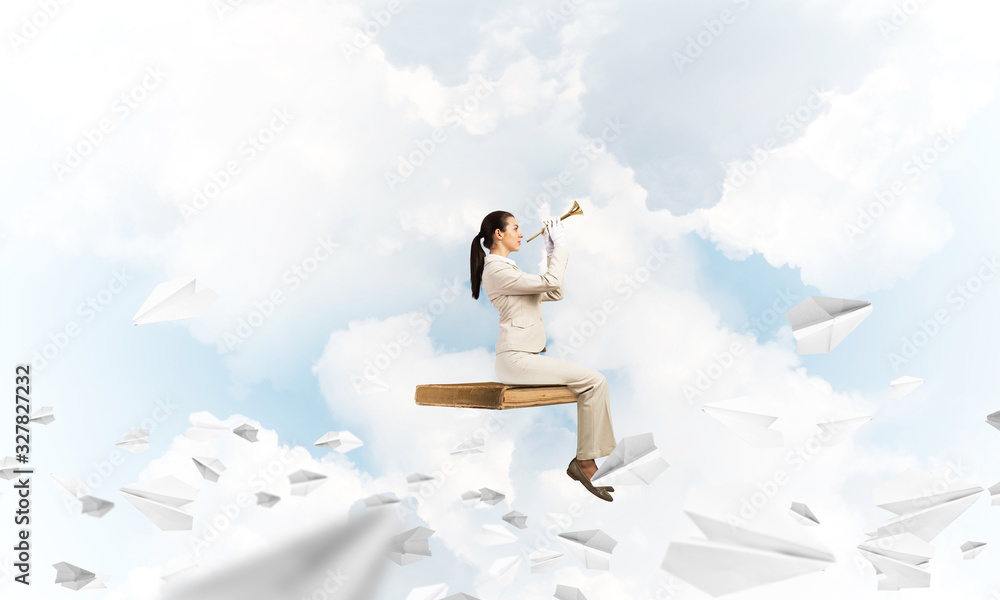 Young woman playing trumpet and sitting on book Young woman playing trumpet and sitting on book