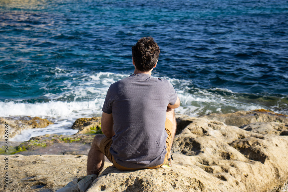 Young man sitting on a rock by the sea. Summer vacation. Mediterranean Sea.