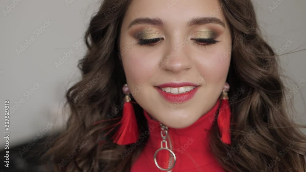 Close Up shot of young beautiful woman in red dress with red brush earrings gorgeous long brunette hair fluttering on wind professional waves hairstyle adorable smile with trendy makeup demonstrates Close Up shot of young beautiful woman in red dress with red brush earrings gorgeous long brunette hair fluttering on wind professional waves hairstyle adorable smile with trendy makeup demonstrates