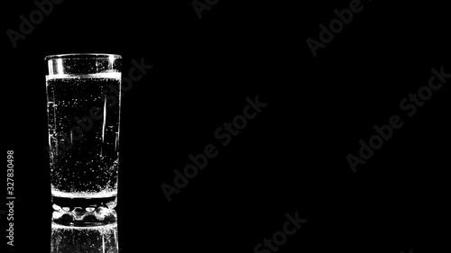 A glass of water on a black background and a bright light close-up. 