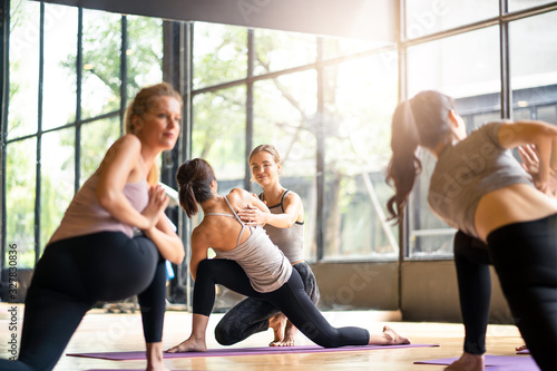 Group of multi ethnics people learning Yoga class in fitness club. Female Caucasian instructor woman coaching and adjust correct pose to Asian girl student at front while others doing follow them.