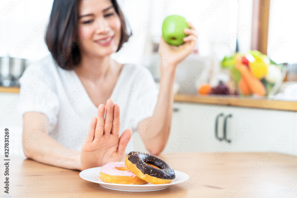 Young girl rejecting junk food or unhealthy food such as donuts and choosing healthy food such as a green apple and salad for having a good health. Dieting and good health concept. - obrazy, fototapety, plakaty 