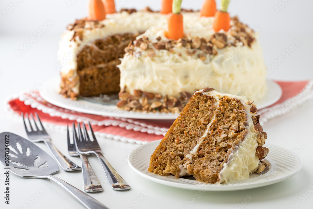 A close up of a carrot cake with cream cheese frosting and a piece of cake in front ready for eating.