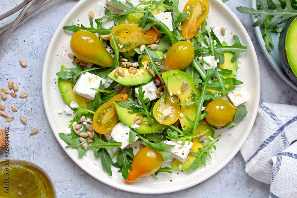 Avocado salad with yellow tomato, feta cheese, arugula and sunflower seeds. Top view with copy space. Healthy food.