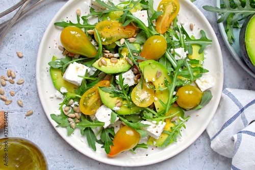Avocado salad with yellow tomato, feta cheese, arugula and sunflower seeds. Top view with copy space. Healthy food.