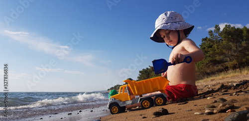 a little boy playing with toy truck and shovel on the beach on a hot summer day photo