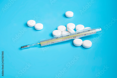 thermometer and white pills on the blue background