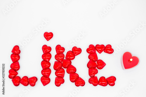 The word  like  is lined with red glass hearts on a white background  on the right - a lighted candle in the shape of a heart. The concept of social networks  approval  support