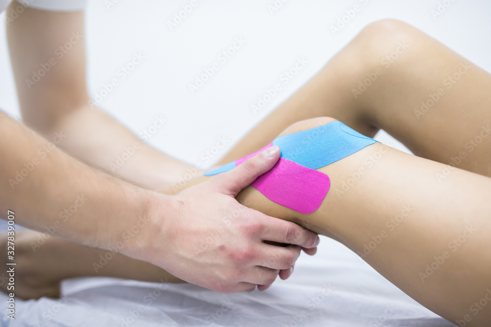 Man physiotherapist is applying kinesio tape to a patient's leg Man physiotherapist is applying kinesio tape to a patient's leg