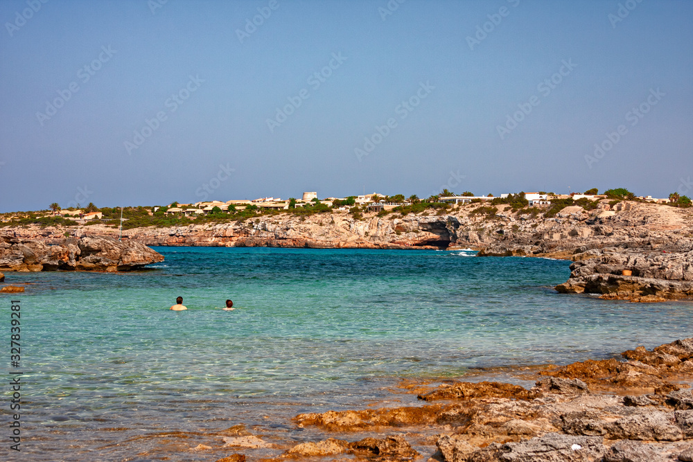 Some tourists bathe in the clear and blue waters of a bay in Formentera in the Balearic islands of Spain.