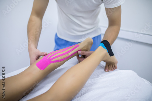 Manual, physio and kinesio therapy techniques performed by a male physiotherapist on a training plastic spine and a female patient leg