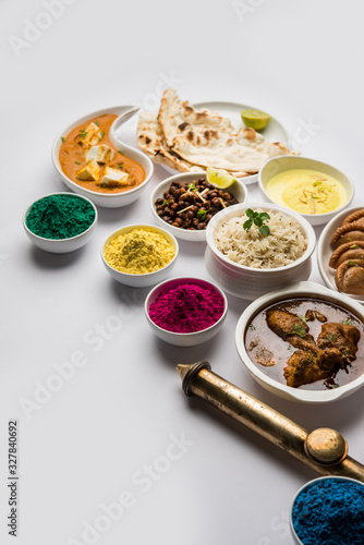 Happy Holy concept  showing Indian assorted lunch food like chicken, paneer butter masala, naan, jeera rice, black chana fry, jalebi, fujiyama, thandai and Farsan with holi colours and pichkari 