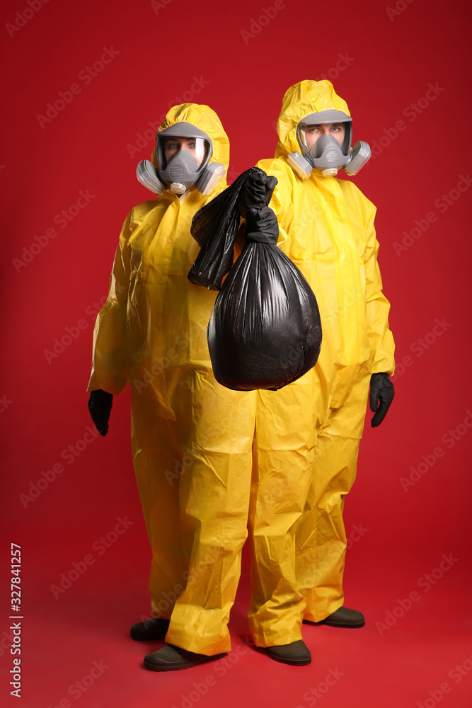 Man and woman in chemical protective suits holding trash bag on red background. Virus research Man and woman in chemical protective suits holding trash bag on red background. Virus research