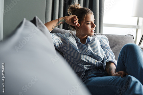 Image of serious caucasian woman looking aside while sitting on sofa