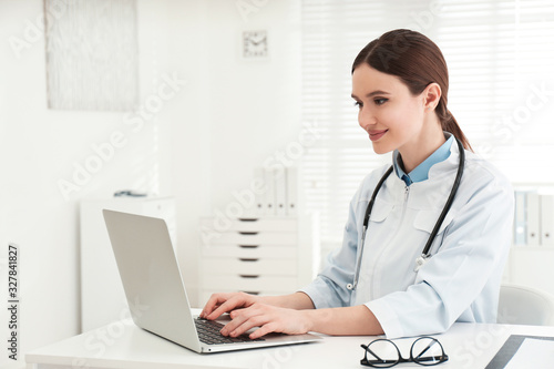 Young female doctor working with laptop at table in office