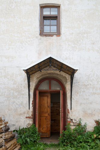 A door with a forged visor and a window in the wall of an old house on a summer morning in the countryside.