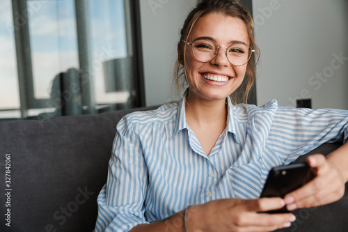 Image of happy young woman in eyeglasses smiling and using cellphone photo