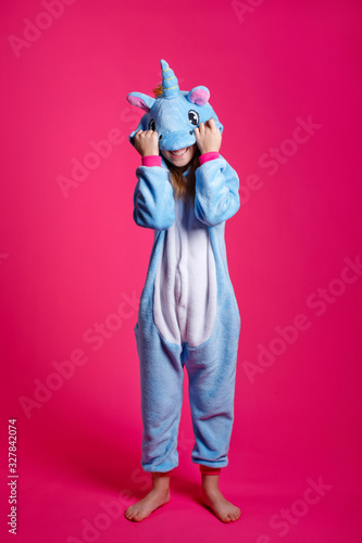 Charming girl playfully poses in the costume of the unicorn. Studio shot of an emotional woman in kigurumi having fun on a pink background.