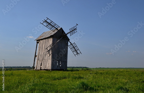 old wooden four-bladed windmill with clouds in a field at summer