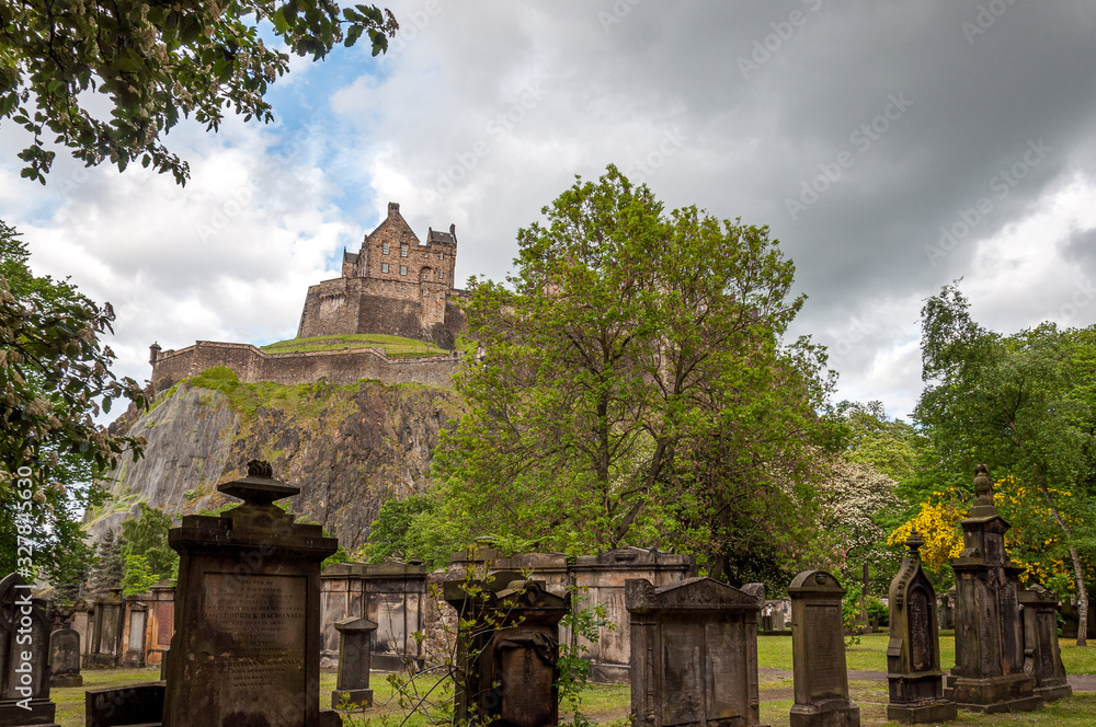 Ancient graveyard tombs with Edinburgh Castle in the background silhouetted against a cloud-laden sky. Concept: famous castles of Scotland