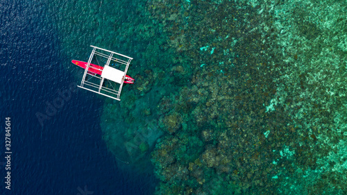 Aerial top down view of boat moving in open sea with clear and turquoise water on over coral reef,  Boat left the tropical lagoon, Moalboal, Oslob, Cebu Island, Philippines.