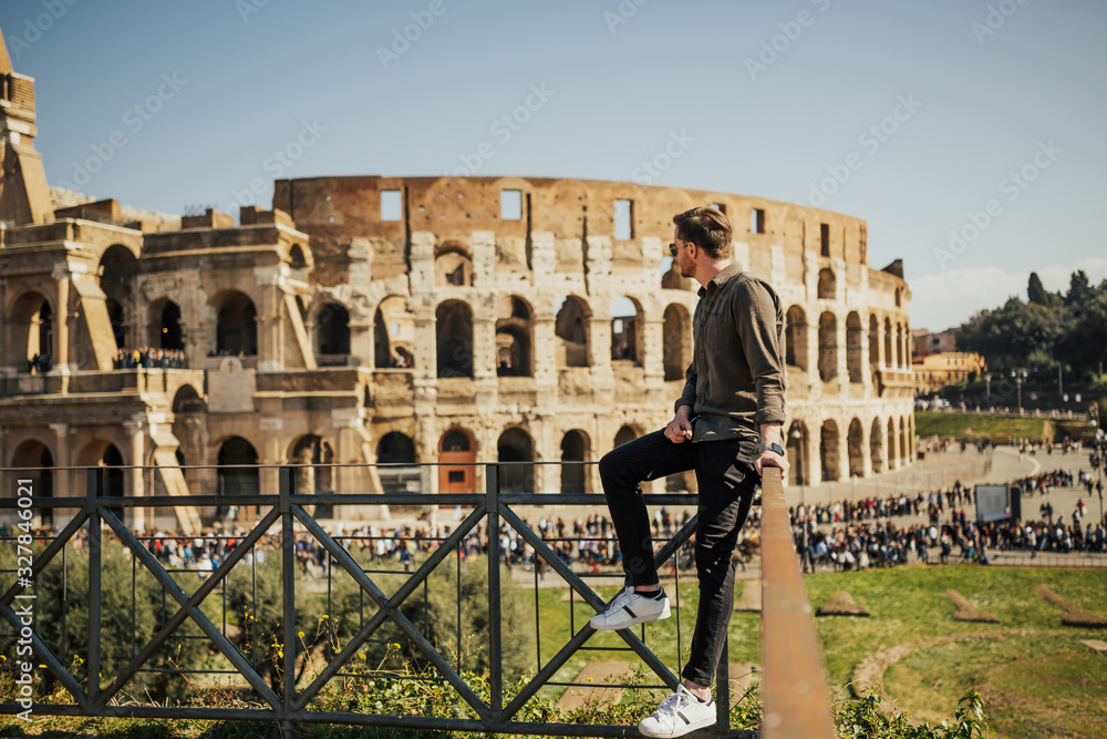 Male tourist wearing stylish clothes and standing near Colosseum in background in Rome, Italy. Concept of traveling to ancient Europe, landmarks and tourists.
