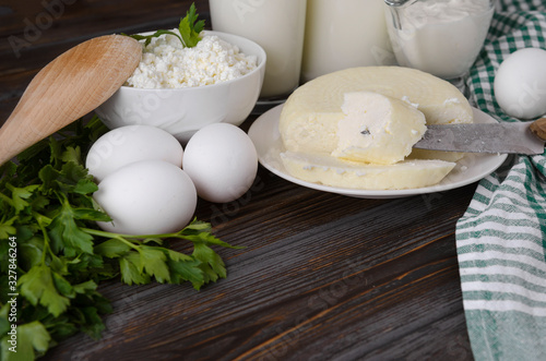 head of cheese, a piece of cheese on a knife, a plate of cottage cheese, 3 white raw eggs, parsley on a wooden