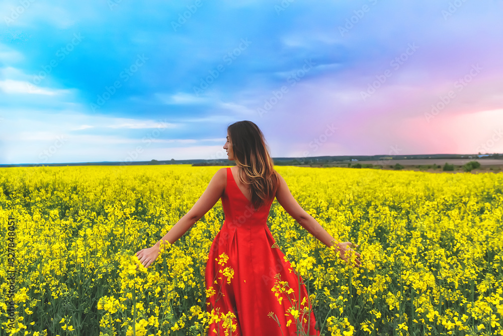 Young beautiful girl in a red dress close up in the middle of yellow field with radish flowers at sunset time Young beautiful girl in a red dress close up in the middle of yellow field with radish flowers at sunset time