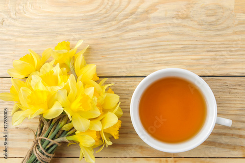 Spring flowers, yellow daffodils and a cup of tea on a natural wooden background. place for text