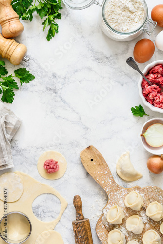 Cooking homemade dumplings or ravioli with meat on a marble table. Traditional russian pelmeni. Flat lay recipe with ingredients. Culinary concept. Space for text