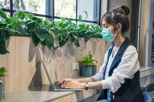 Pretty Asian blogger wear protective masks prevent PM 2.5 and corona viruus or covid 19 at co working space modern office .Freelance and Health concept.