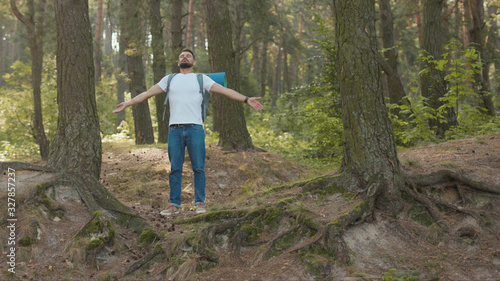 Portrait young man with backpack stand rises hand feel freedom in the forest look around at sunlight nature alone hiking woods activity young vacation attractive autumn hiker travel slow motion