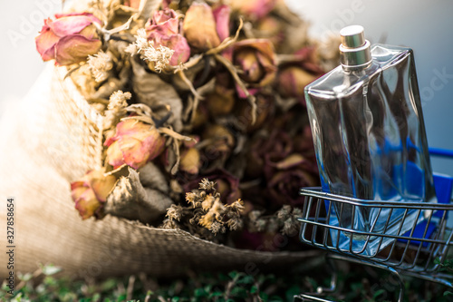 background view of a clear bottle containing perfume placed near a bouquet of roses on the table  business concept selling products or cosmetic products