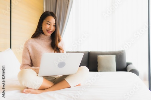 Portrait beautiful young asian woman using laptop with mobile phone on bed