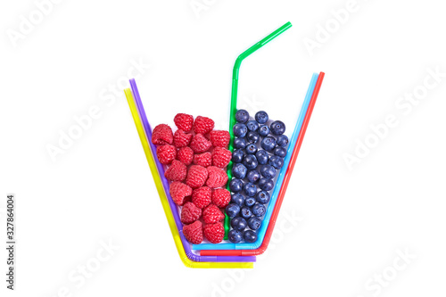 Composition of multi-colored cocktail tubes and berries isolated on white. Raspberries and blueberries in a glass. Creative illustration of healthy food or drink