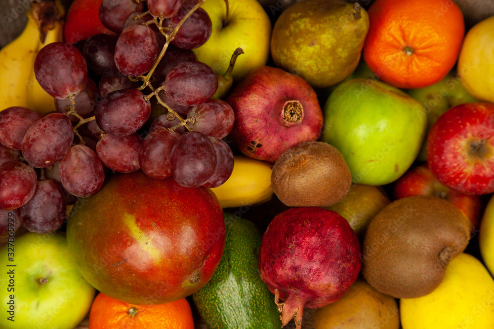 Fruit basket with different fruits. Vitamin set of a healthy diet. Fruit isolated on a gray background. Large set of fruits on a wooden kitchen table. Bananas, apples, pears, pomegranate, tangerine.