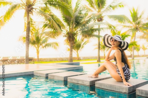Portrait beautiful young asian woman relax around outdoor swimming pool in hotel resort with palm tree at sunset or sunrise © siraphol