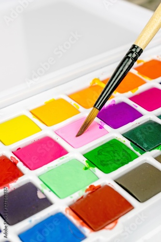 An artists paint brush and a box of colourful water colour paints