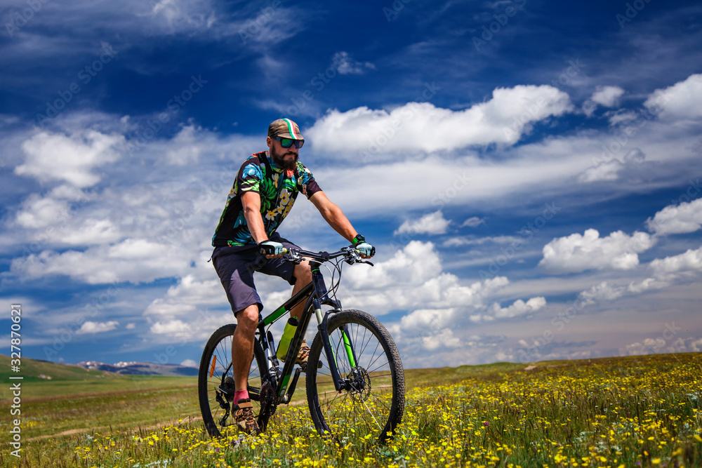 A cyclist rides in the mountains among flowering fields. Bike tour to outdoor. Alpine Song-Kul Lake. Kyrgyzstan