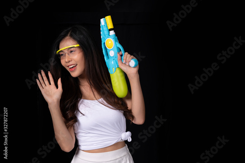 Portrait cheerful young asian woman with red glasses holding plastic water gun on balck background. Songkarn festival, Thailand. Thai New Year's Day. Isolated black background.