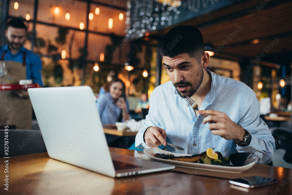 man using laptop while having lunch in restaurant man using laptop while having lunch in restaurant