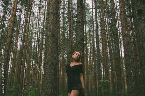 Portrait of young beautiful girl in forest that leans on tree trunk