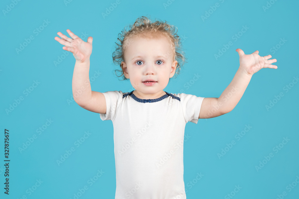 Cute curly baby girl of two years raises her hands up on a blue background Cute curly baby girl of two years raises her hands up on a blue background