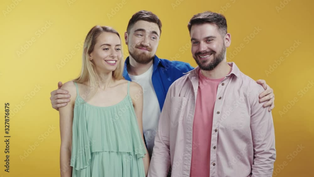 Caucasian young couple of lovers holding hands posing on background. Third wheel jealous bearded friend embracing separating man and woman. Love triangle. Caucasian young couple of lovers holding hands posing on background. Third wheel jealous bearded friend embracing separating man and woman. Love triangle.