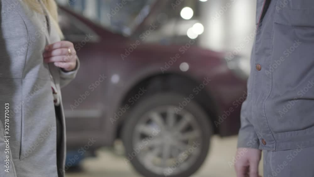 Close-up of Caucasian woman and man shaking hands in car repair shop. Successful businesswoman and professional maintenance engineer making deal at service station. Insurance, maintenance, handshake. Close-up of Caucasian woman and man shaking hands in car repair shop. Successful businesswoman and professional maintenance engineer making deal at service station. Insurance, maintenance, handshake.