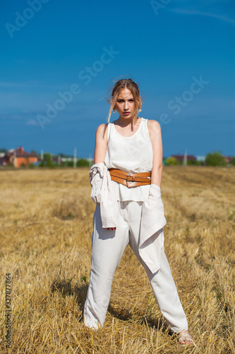 Young woman in a beige suit posing on a background of haystacks in a cut field.