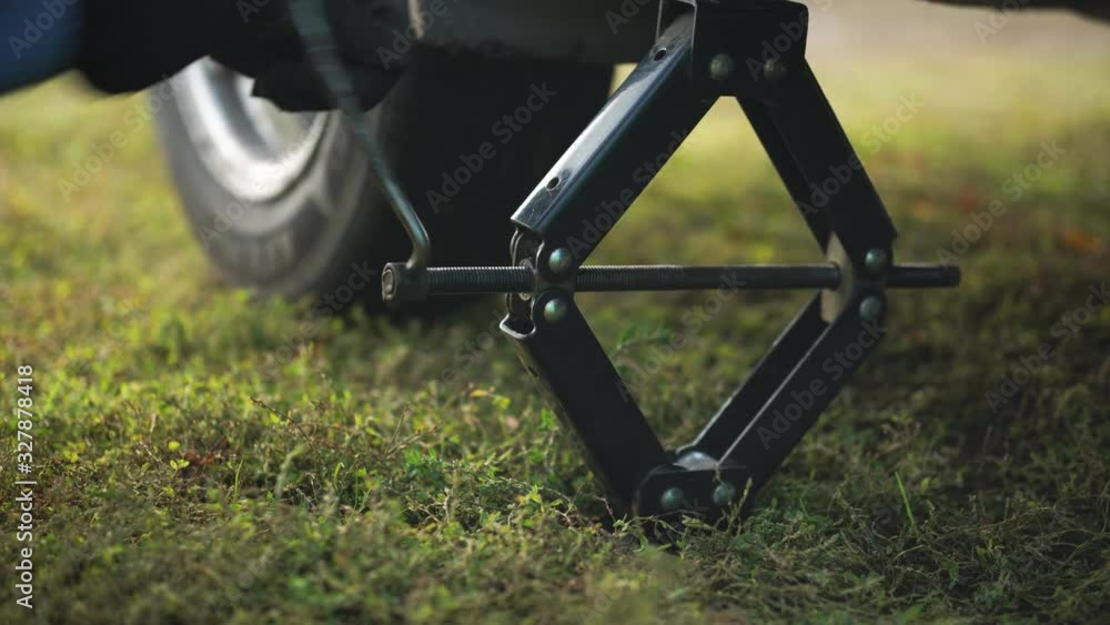 A man lowers a car using a jack. Car repair in the summer on the road. 4K video. A man lowers a car using a jack. Car repair in the summer on the road. 4K video.