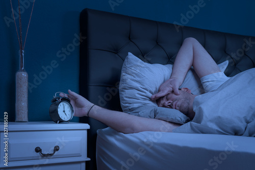 man looks at his alarm clock at night and cannot sleep